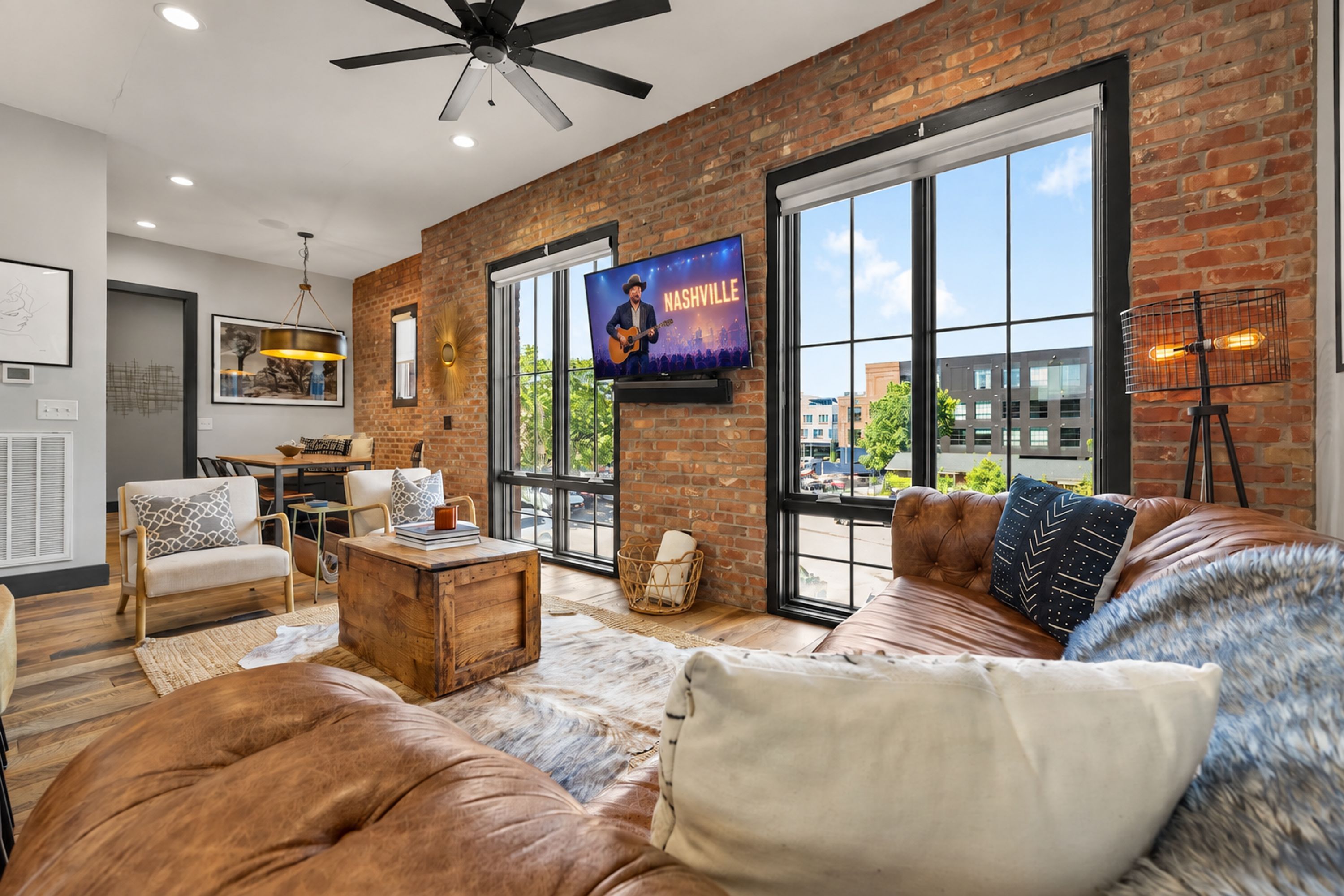 A spacious living room with a large TV, leather sofas, and a brick wall.