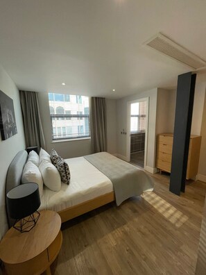 A modern bedroom with a bed, a bedside table, a window with curtains, and a view of the outside. - City Double VII - Stylish 2BR Home in the City (London)