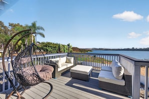 A deck with outdoor furniture, including a hanging chair and sofas, overlooking a body of water. - Lagoonfront 3BR Pickleball Kayaks Basketball (Carlsbad)