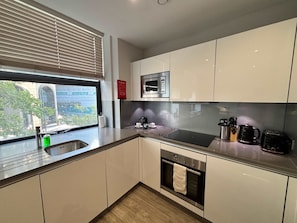 A modern kitchen with a stainless steel sink, a microwave, a stovetop, and a built-in oven. - City Tower - Stylish 1BR Home in the City (London)