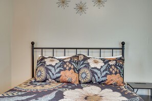 Uma cama com colcha estampada e duas almofadas, mesa de cabeceira e detalhes decorativos nas paredes.