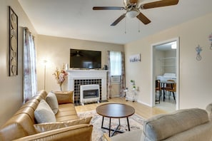 Uma sala de estar com sofá, lareira, ventilador de teto e uma área de jantar com cadeiras e mesa.
