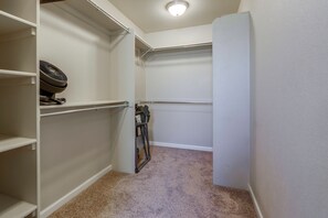 A walk-in closet with white shelving, a fan, and a folded chair.
