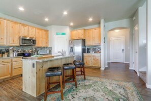 A kitchen with wooden cabinets, stainless steel appliances, a central island with stools, and a patterned rug.