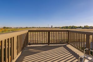 A wooden deck with a view of a grassy field and distant buildings.