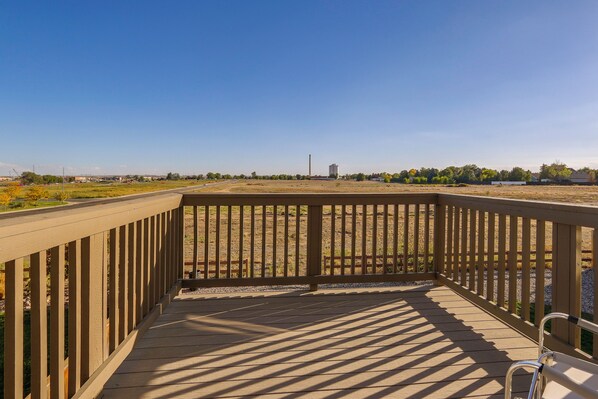 Une terrasse en bois offrant une vue sur un champ verdoyant et des bâtiments situés au loin.