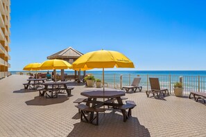 Een terras buiten met honingraat betegelde vloer, gele parasols, houten tafels en loungestoelen.