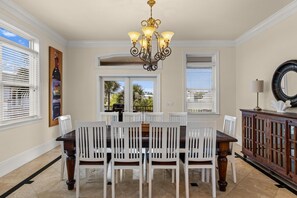 Ein Esszimmer mit einer Chandelier, weißen Stühlen, einem Holztisch und Blick durch die Fenster.