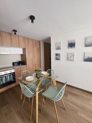A modern kitchen with wooden cabinets, a glass dining table with chairs, and a wall with framed artwork. - Marvelous 2-bedroom apartment in peaceful Ñuñoa neighborhood (Ñuñoa)