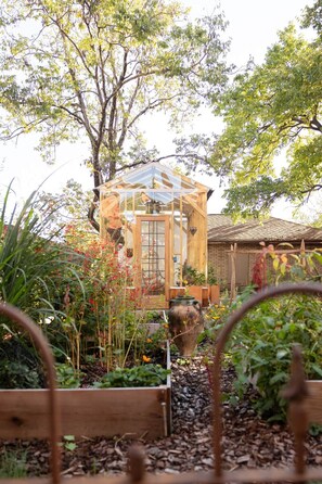 A wooden structure with a glass roof, surrounded by a garden with various plants and flowers.