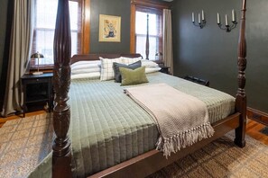 A four-poster bed with a quilted bedspread, a throw blanket, and multiple pillows.