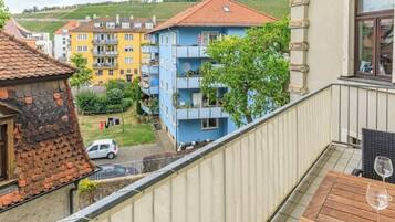 Ein Balkon mit Tisch und Weinglas, mit Blick auf ein Wohngebiet mit farbenfrohen Gebäuden und einem geparkten Auto auf der Straße.