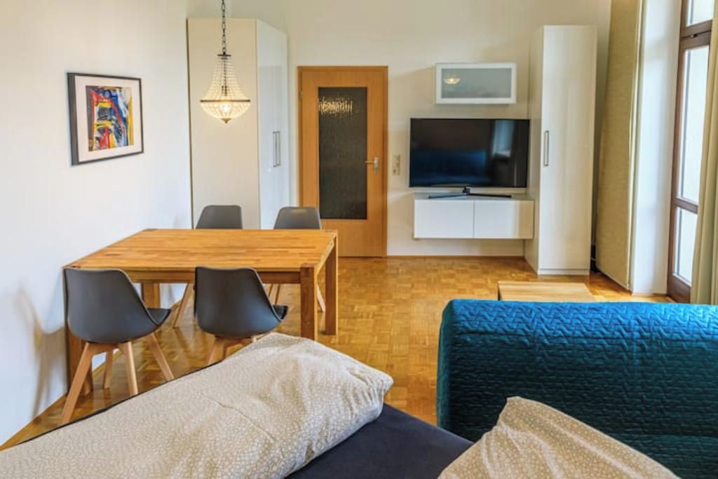Ein modernes Wohnzimmer mit einem Holzesstisch, schwarzen Stühlen, einem blauen Sofa und einem Fernseher auf einem Schrank.