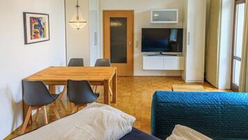 Ein modernes Wohnzimmer mit einem Holzesstisch, schwarzen Stühlen, einem blauen Sofa und einem Fernseher auf einem Schrank.