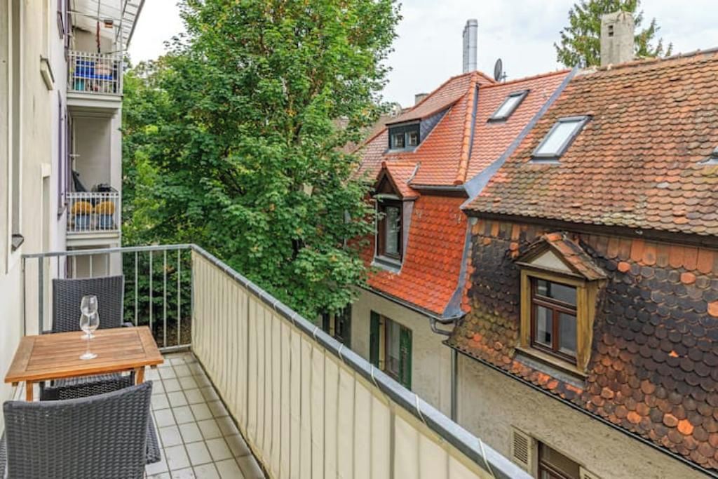 Een balkon met een tafel en stoelen, uitzicht op omliggende gebouwen en een boom.
