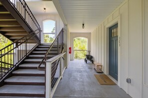 Eine überdachte Veranda mit einer Treppe zu einer oberen Ebene, einer Fußmatte und einer Tür mit einer Hausnummer.