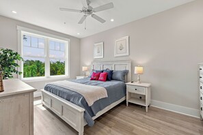 Ein Schlafzimmer mit einem Bett, Nachttischen, einem Deckenventilator, einem Fenster mit Blick und einer Kommode.
