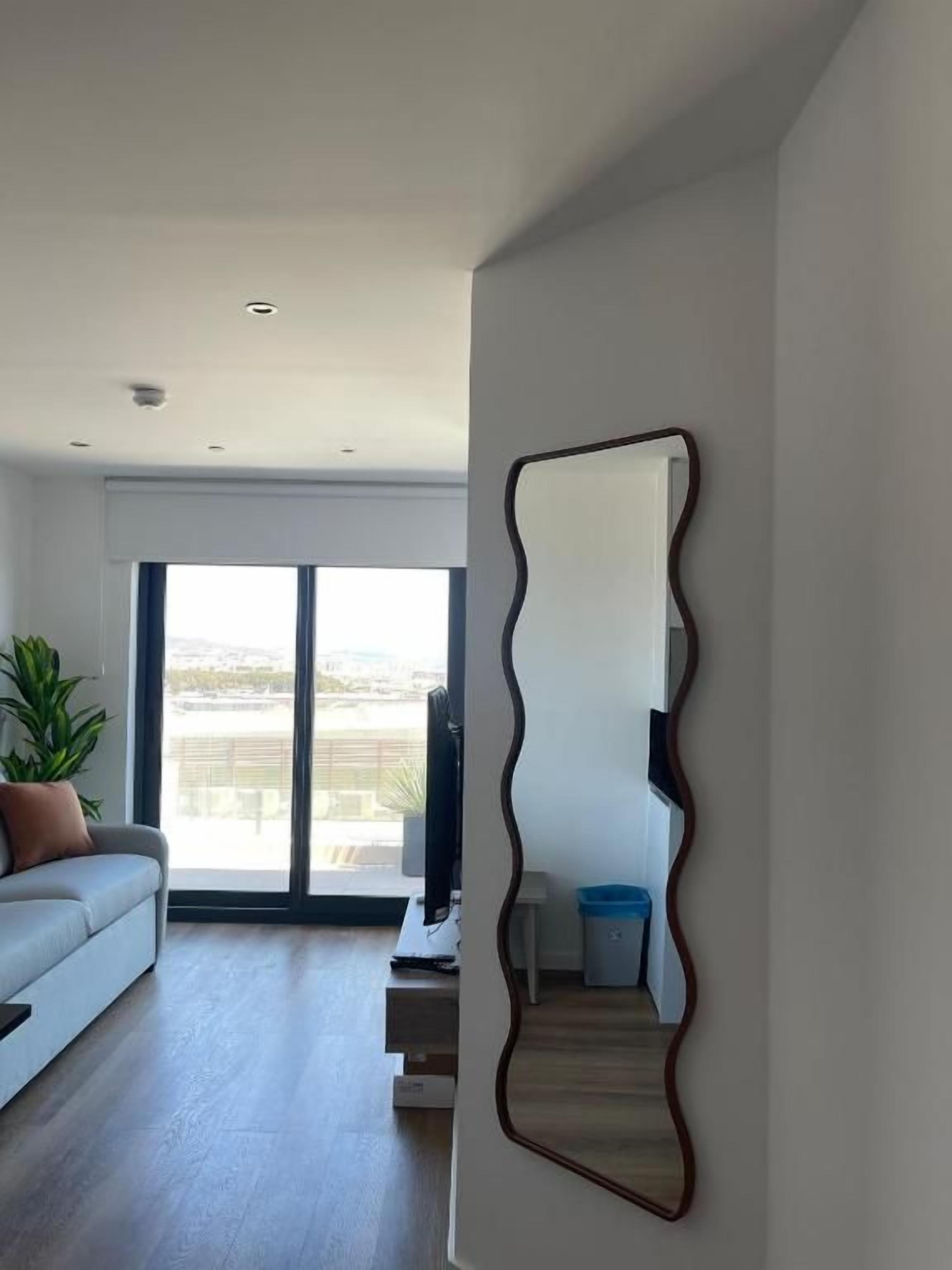 A modern living room with a large mirror, a sofa, a coffee table, and a view through a large window.