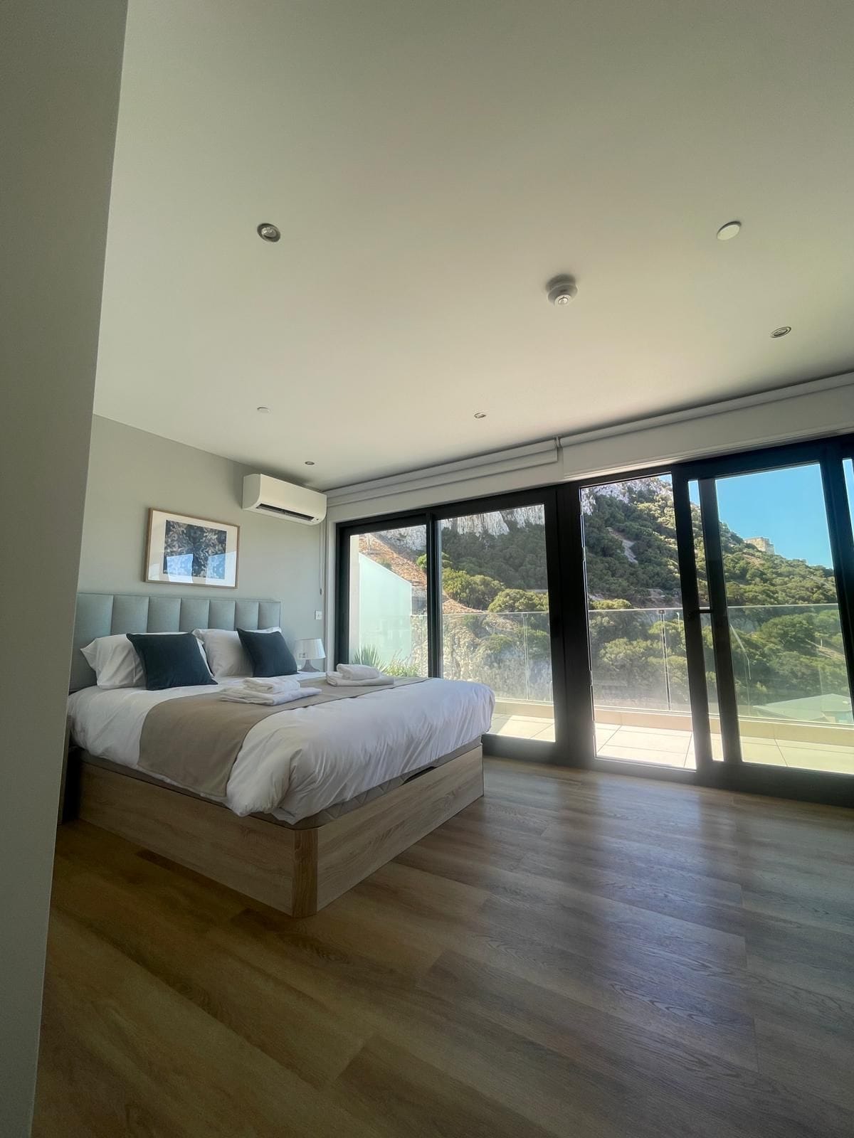 A modern bedroom with a large bed, a view of a mountainous landscape, and a sliding glass door leading to an outdoor area.