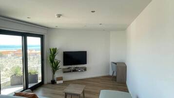 Ein modernes Wohnzimmer mit großem Fenster, Flachbildfernseher und einer Couch.