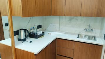 Una cocina moderna con salpicadero de mármol, armarios de madera, un lavamanos de acero inoxidable y un hervidor en la encimera.