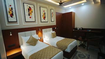 Habitación de hotel con dos camas, un escritorio, un armario y cuadros en la pared.