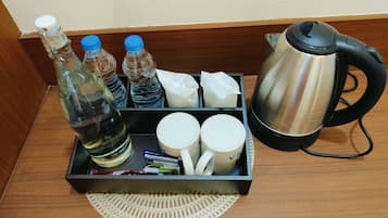Mesita de noche en una habitación de hotel con una botella de agua, dos botellas adicionales, una caja de pañuelos, una taza, un hervidor y una pequeña bandeja con una servilleta.
