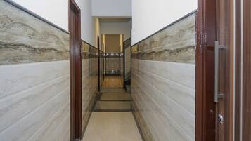 A corridor with marble walls, a wooden door, and a staircase leading to an upper floor.