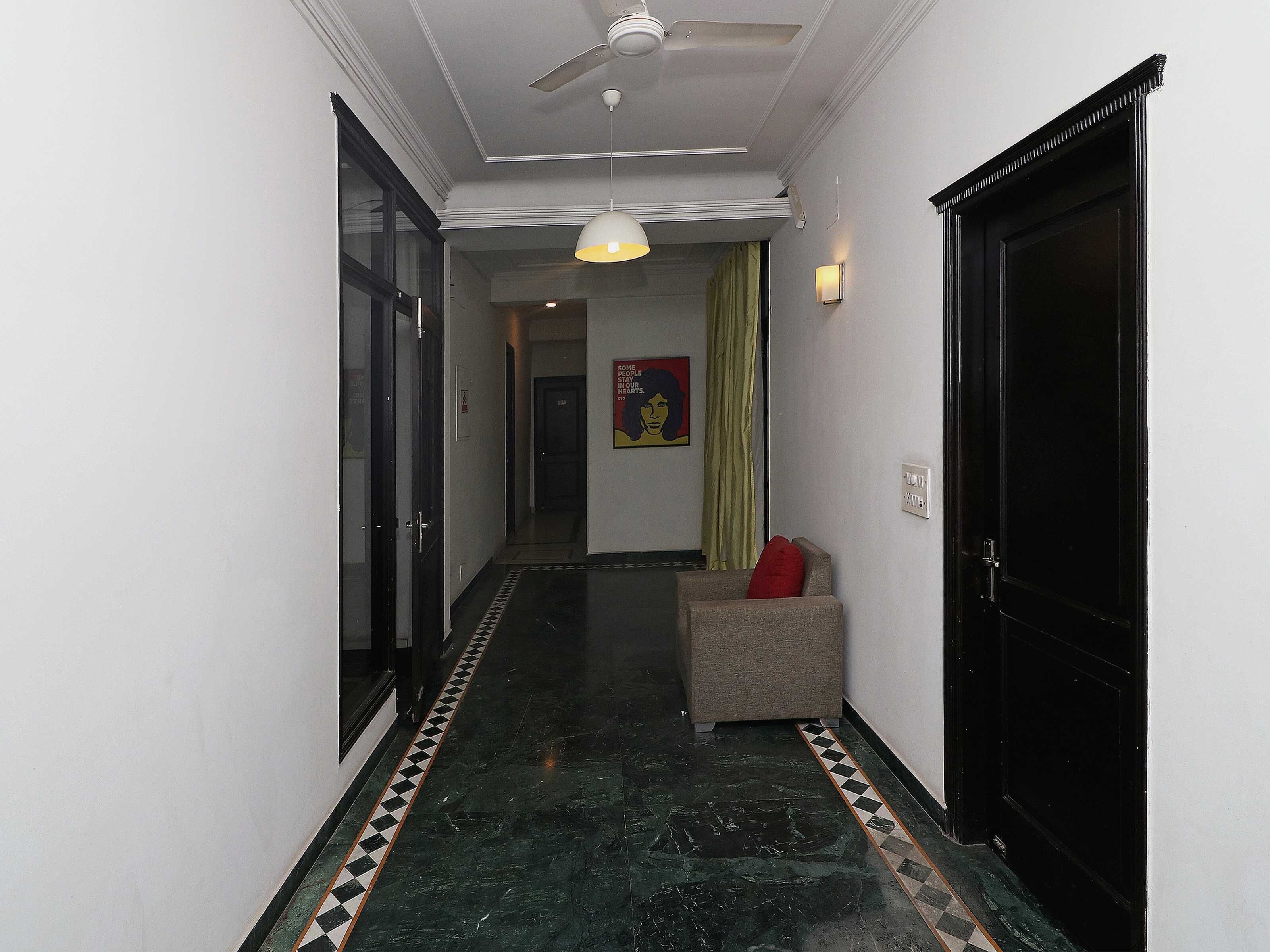 A hallway with a ceiling fan, a patterned floor, a door with a black frame, and a small seating area with a red cushion.