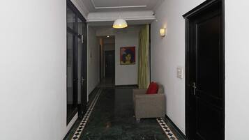 A hallway with a ceiling fan, a patterned floor, a door with a black frame, and a small seating area with a red cushion.