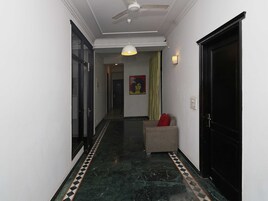 A hallway with a ceiling fan, a patterned floor, a door with a black frame, and a small seating area with a red cushion.