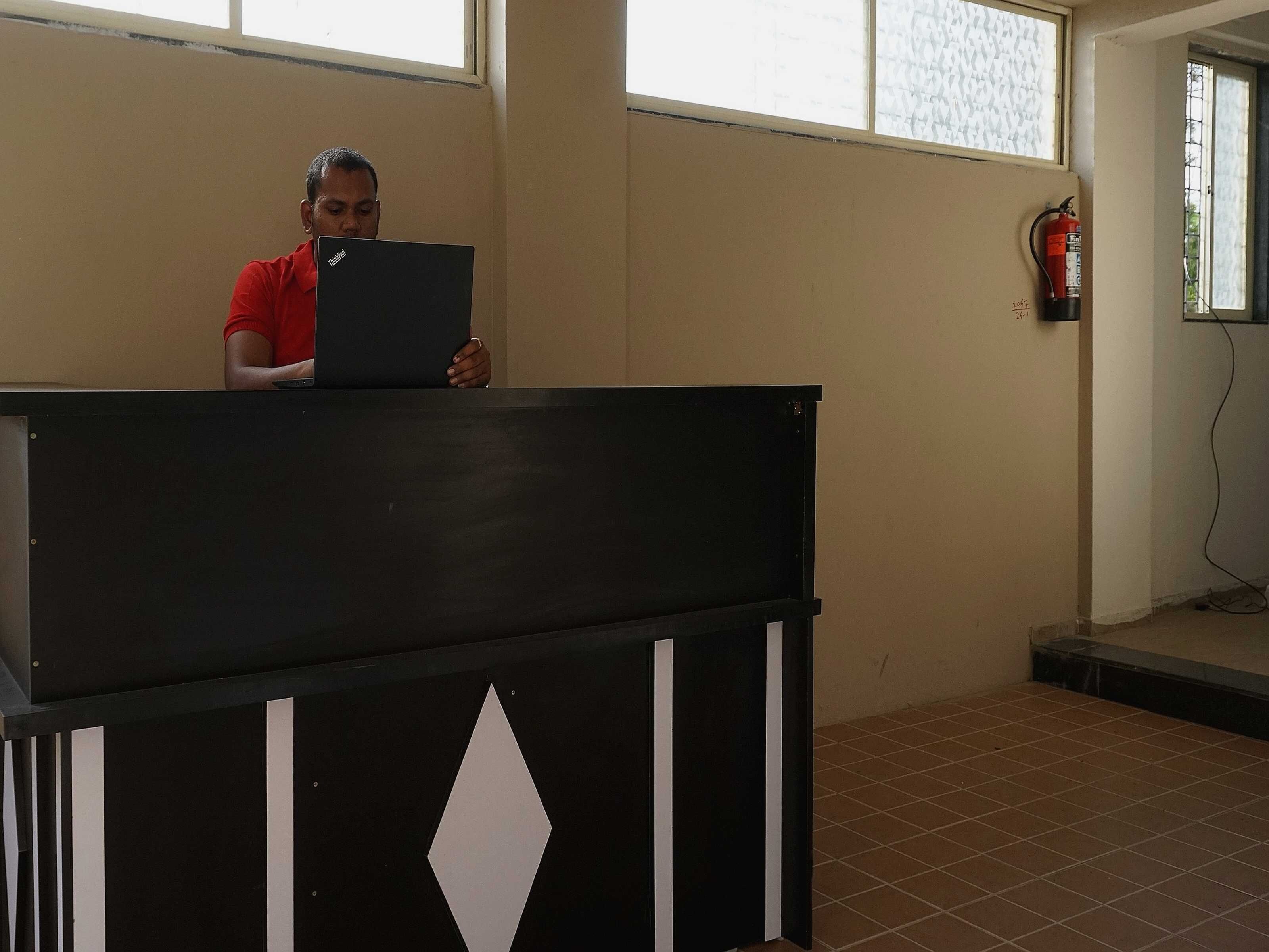 A person standing behind a podium in a room with tiled flooring and a window.