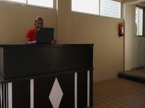 A person standing behind a podium in a room with tiled flooring and a window. - OYO 37456 Arusai (Paud)
