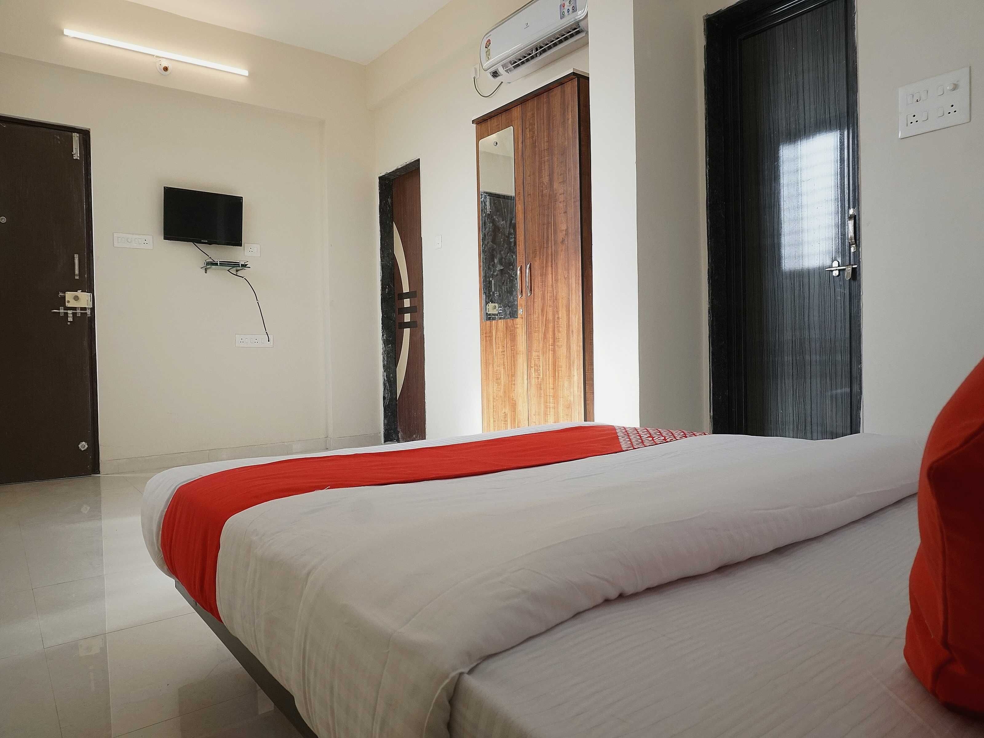 A hotel room with a bed, a television, an air conditioning unit, and a wardrobe.