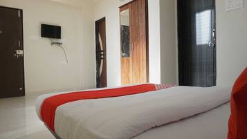 A hotel room with a bed, a television, an air conditioning unit, and a wardrobe.