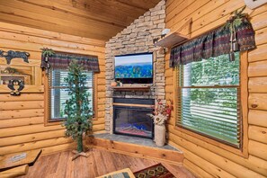 Ein Blockhaus-Interieur mit Kamin, einem darüber montierten Fernseher und einem Weihnachtsbaum.