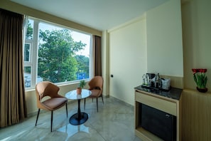 A small, modern room with two chairs, a round table, a potted plant, a coffee machine, and a cabinet. - Emerald Signature (Mysore)
