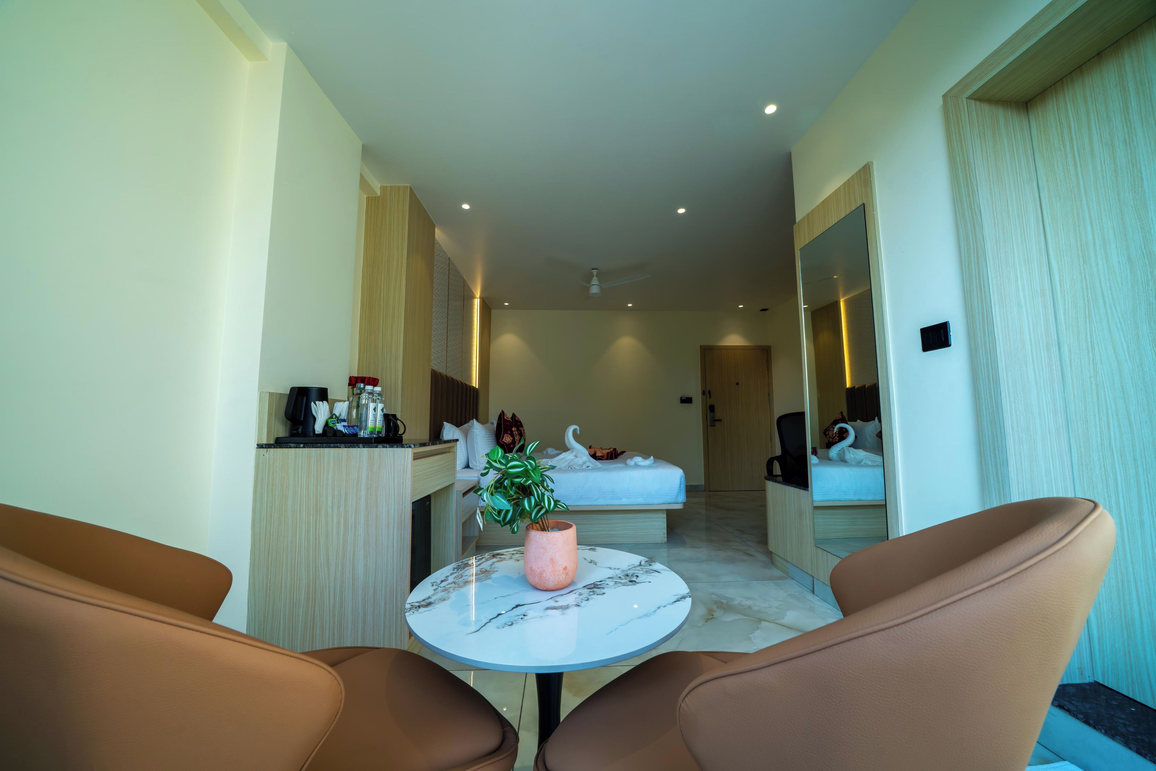 A hotel room with a bed, a small table with chairs, a mirror, and a plant.