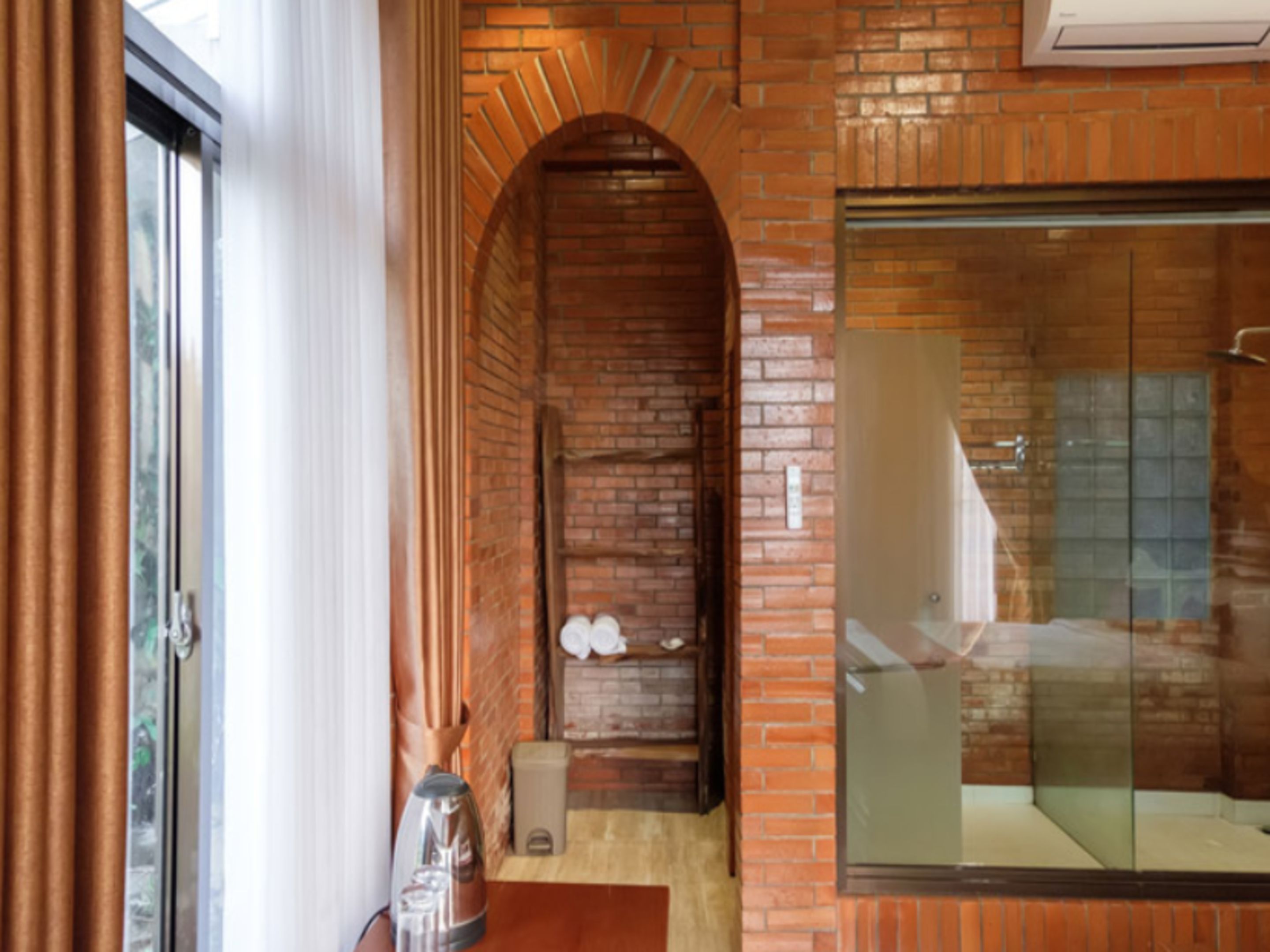 A bathroom with a glass shower enclosure, a brick wall, and a wooden bench.