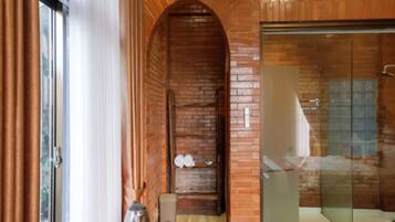 A bathroom with a glass shower enclosure, a brick wall, and a wooden bench.