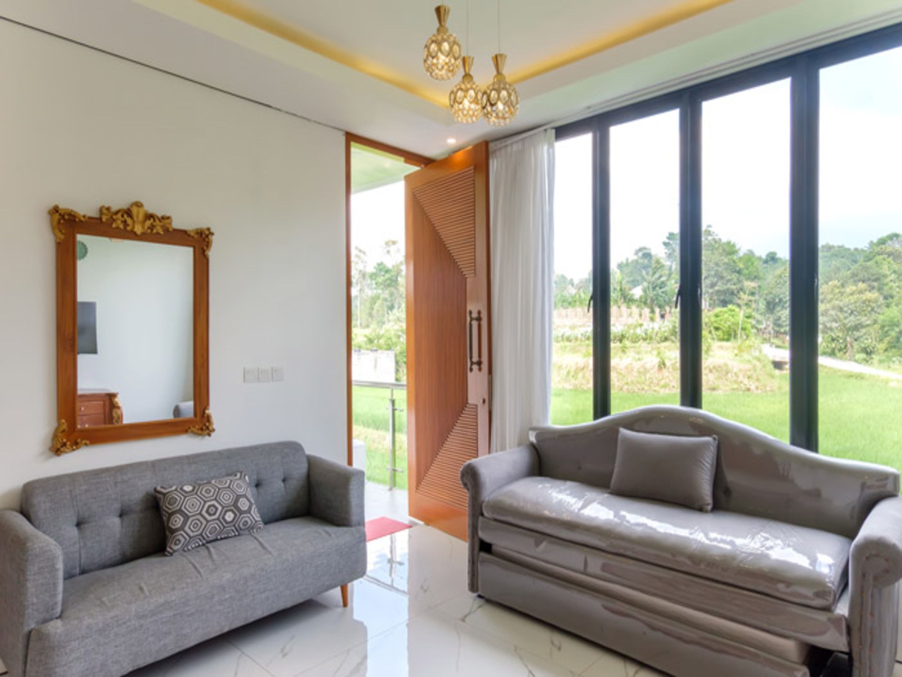 A modern living room with two sofas, a large mirror, and a view of a green landscape through large windows.