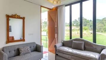 A modern living room with two sofas, a large mirror, and a view of a green landscape through large windows.