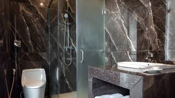 Un baño moderno con ducha envuelta en vidrio, inodoro y lavamanos con encimera de mármol.