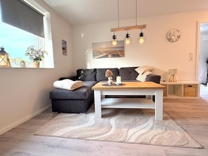 Ein modernes Wohnzimmer mit einem grauen Sofa, einem Holztisch und einem gemusterten Teppich.