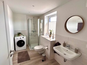 Ein modernes Badezimmer mit Duschkabine aus Glas, Toilette, Waschbecken und Waschmaschine.