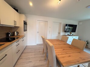 Eine moderne Küche mit Holzschränken, einem eingebauten Backofen und einem Essbereich mit Holztisch und -stühlen.