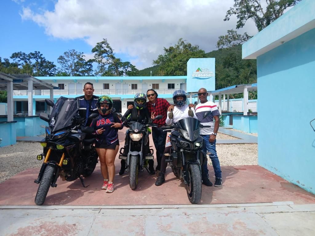 Un grupo de personas posando con motocicletas frente a un edificio de fachada azul y un letrero que dice 'Hotel'.