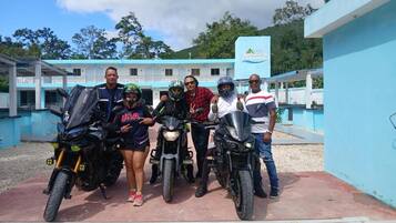 Un grupo de personas posando con motocicletas frente a un edificio de fachada azul y un letrero que dice 'Hotel'.