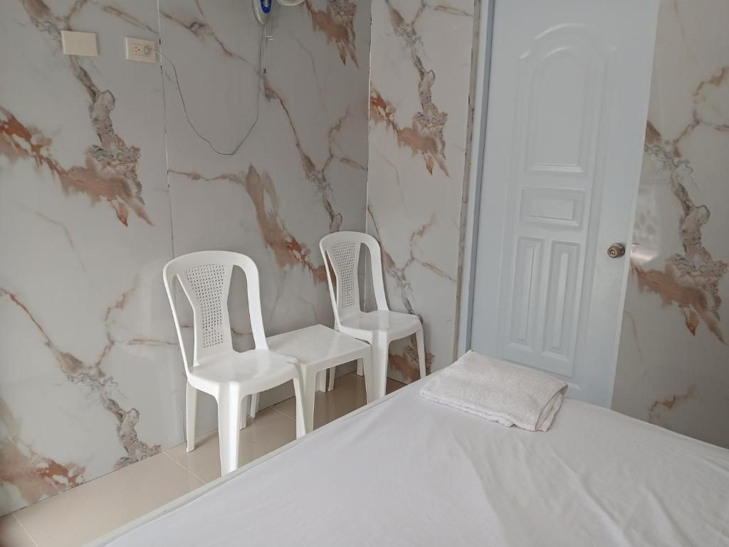 Un dormitorio con cama, dos sillas de plástico blancas, una puerta blanca y paredes con diseño de mármol.