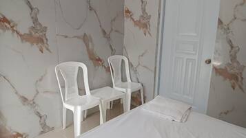 Un dormitorio con cama, dos sillas de plástico blancas, una puerta blanca y paredes con diseño de mármol.